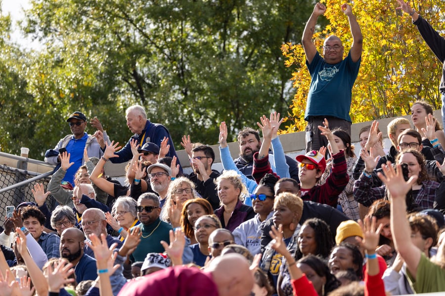 Attendees at the 2023 Homecoming football game cheer by waving their hands. 
