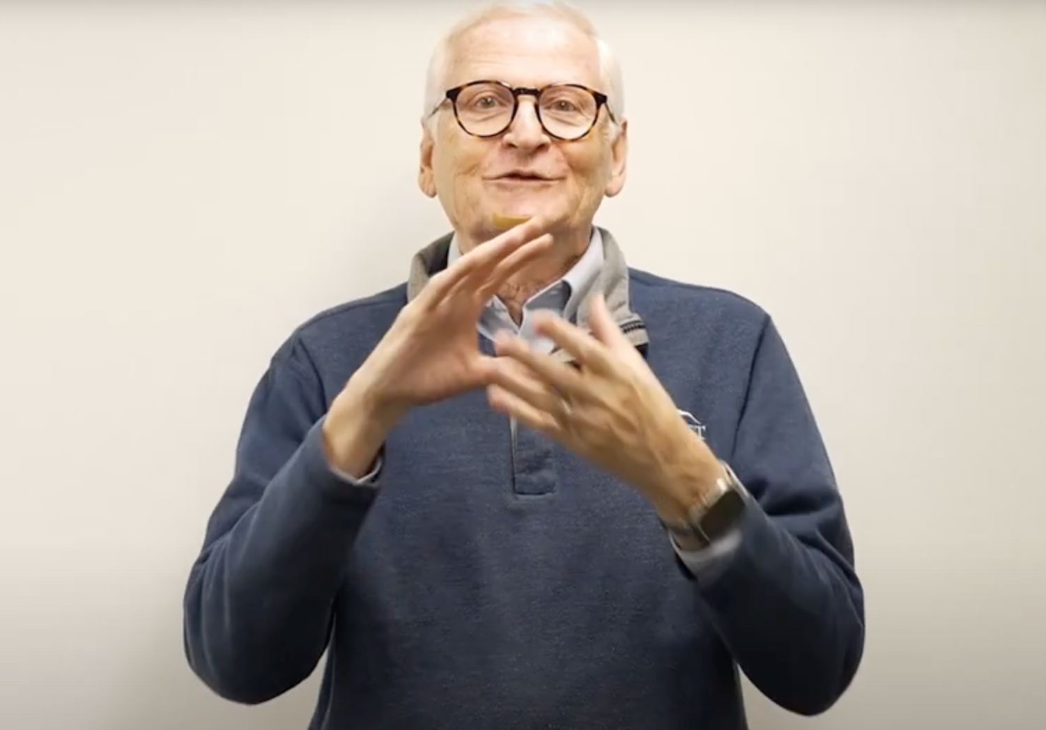 Phil Bravin stands in front of a white background. He is bespectacled and wearing a blue sweater with the Gallaudet logo in the upper right corner.