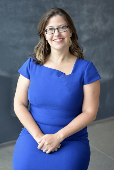 Tawny Holmes-Hlibok faces the camera smiling and wearing a blue dress and 